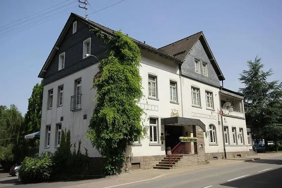 Weißes zweistöckiges Haus mit Efeu, Bogeneingang und Treppe an einer sonnigen Straßenecke