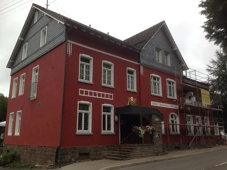 Rotes Gebäude mit weiß umrandeten Fenstern und grauem Dach, von außen an einem bewölkten Tag betrachtet