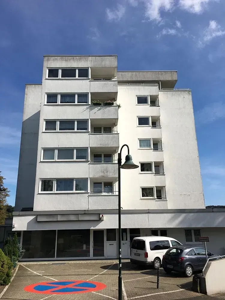 Fünfstöckiges weißes Wohnhaus mit geparkten Autos, einer Straßenlaterne und blauem Himmel.