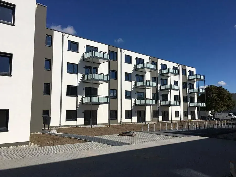 Moderne weiße Wohnhäuser mit Balkonen entlang einer gepflasterten Straße unter klarem blauen Himmel