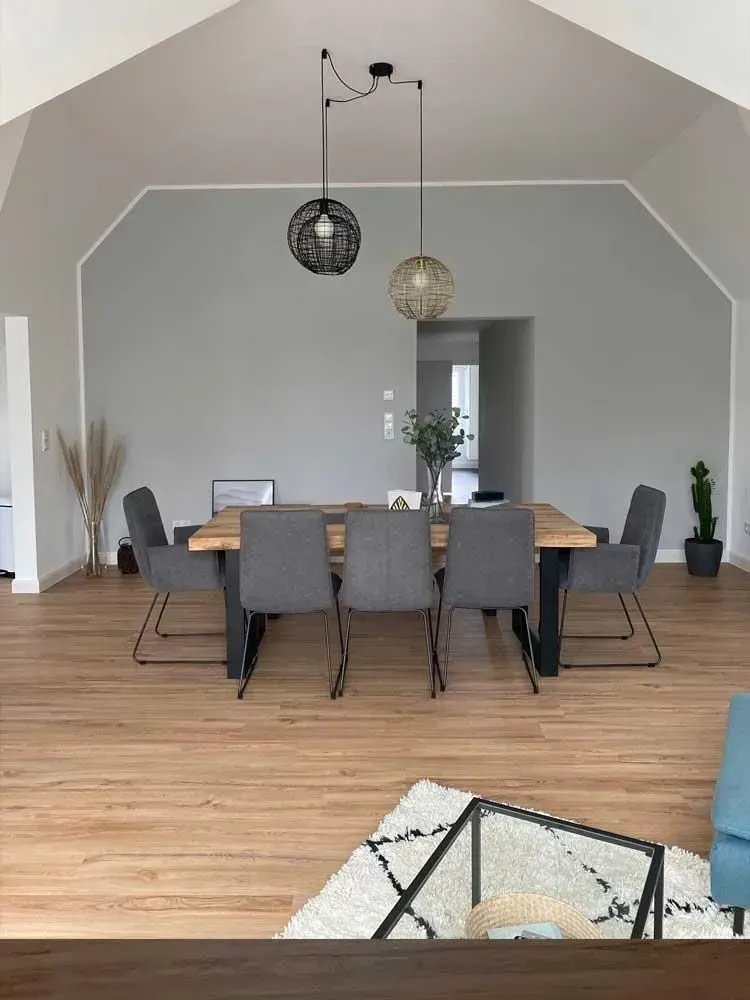 Modernes Esszimmer mit grauen Stühlen, einem Holztisch und schwarz-goldenen Pendelleuchten auf Hartholzboden.
