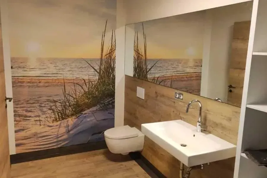 Modernes Badezimmer mit Strandmotiv, wandhängendem WC, Waschbecken und Waschtisch aus Holz in Beigetönen