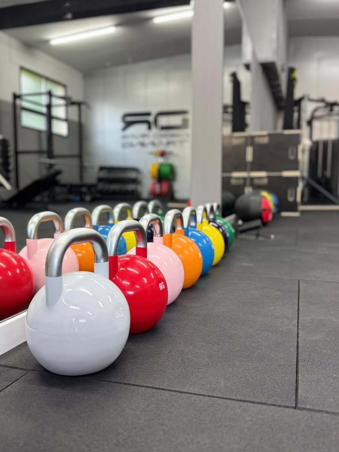 Pesas rusas de colores alineadas en el suelo de un gimnasio, con pesos rojos, blancos, naranjas, amarillos y azules