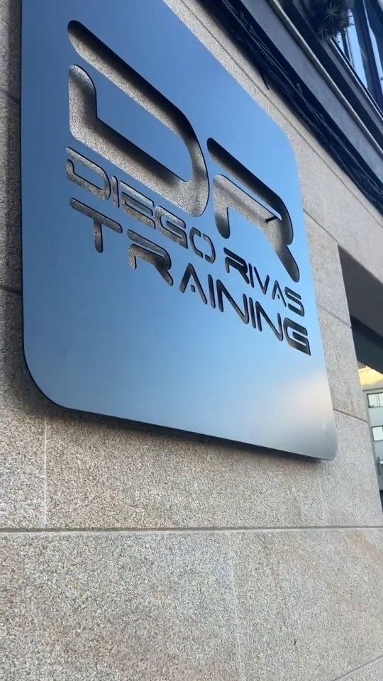 Letrero metálico con la inscripción “DR Training” en la pared exterior de un edificio.