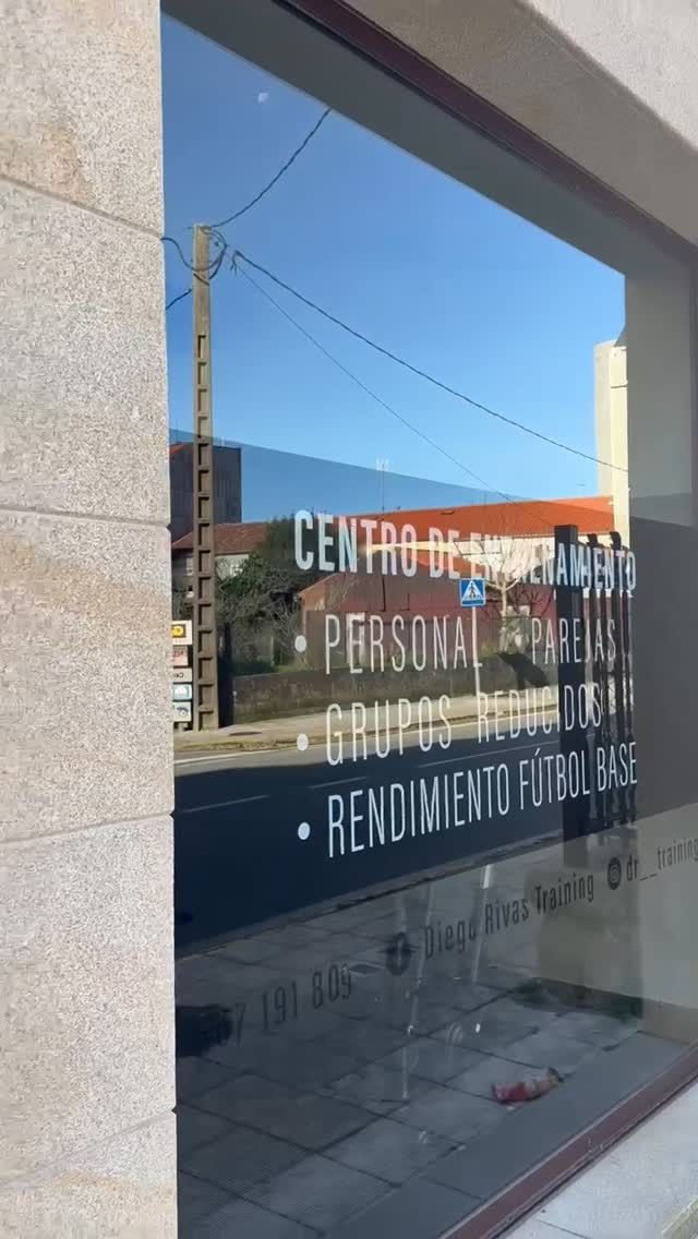 Fachada de cristal con letras blancas para un centro de entrenamiento personal, que refleja la calle exterior.