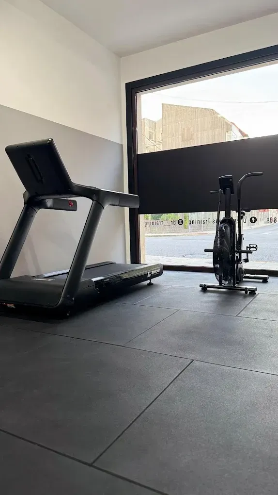Gimnasio minimalista con cinta de correr, bicicleta estática y una gran ventana que deja entrar la luz natural.