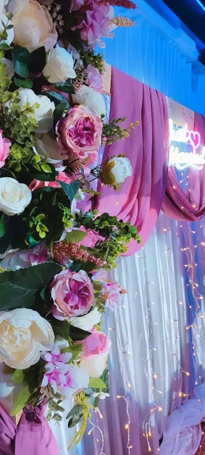 Escenario floral para bodas con cortinas rosas, luces blancas de hadas y arreglos de rosas rosas y blancas.