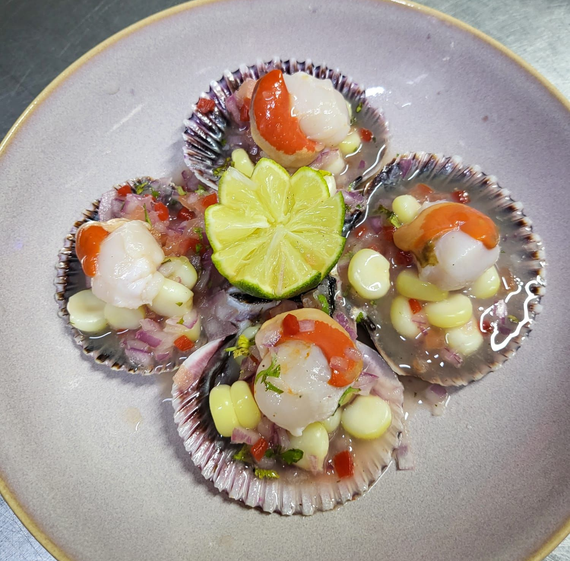Ceviche de mariscos con camarones, mejillones, maíz, cebolla y lechuga en un plato blanco.