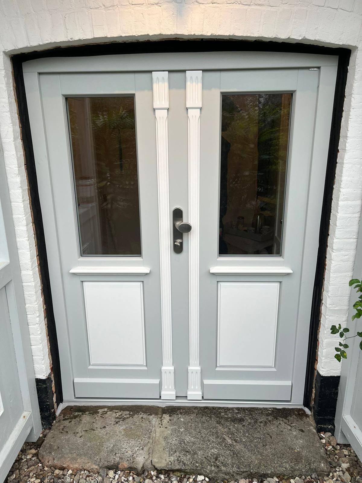 Eine weiße Tür mit zwei Fenstern und einem schwarzen Griff an einem weißen Backsteingebäude.