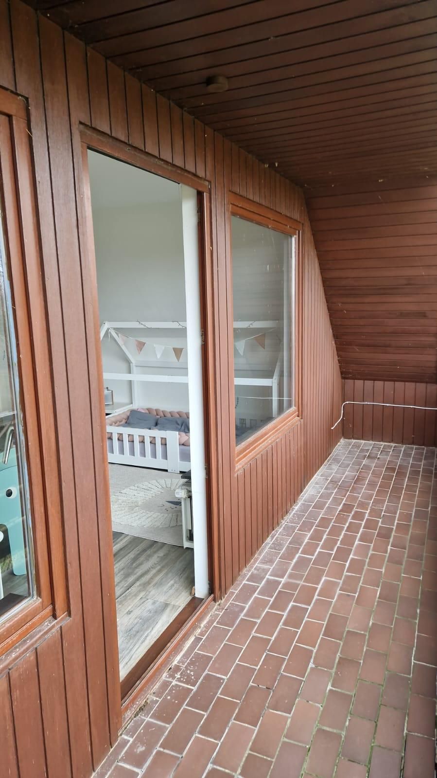 Ein Balkon mit einem Bett und einer Glasschiebetür, die zu einem Schlafzimmer führt.