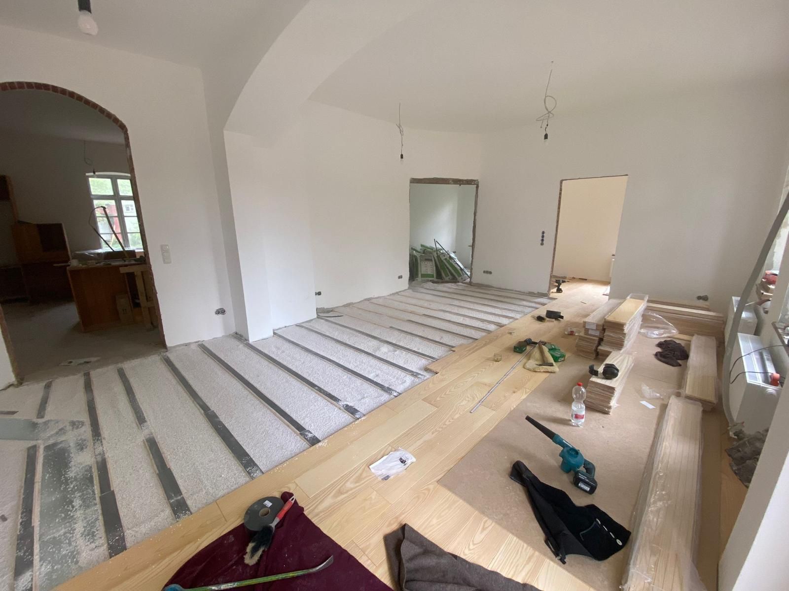 Ein Zimmer mit Holzboden und weißen Wänden wird umgestaltet.