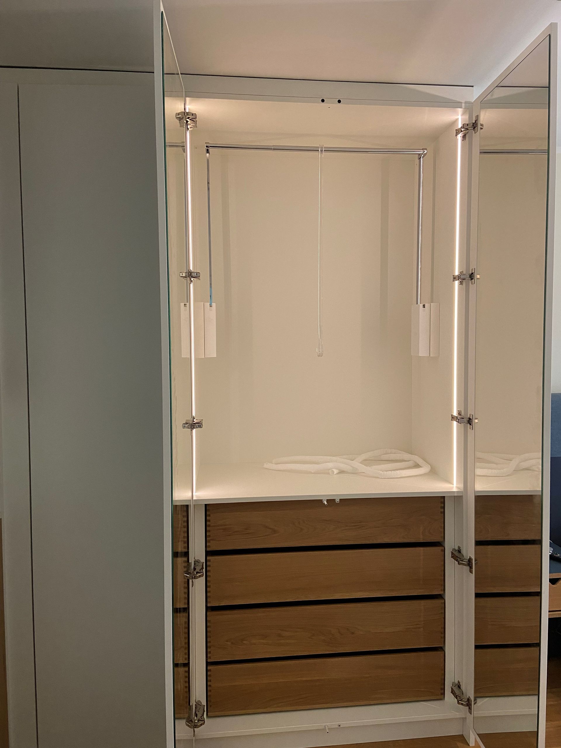 Ein weißer Kleiderschrank mit Holzschubladen und einem Spiegel