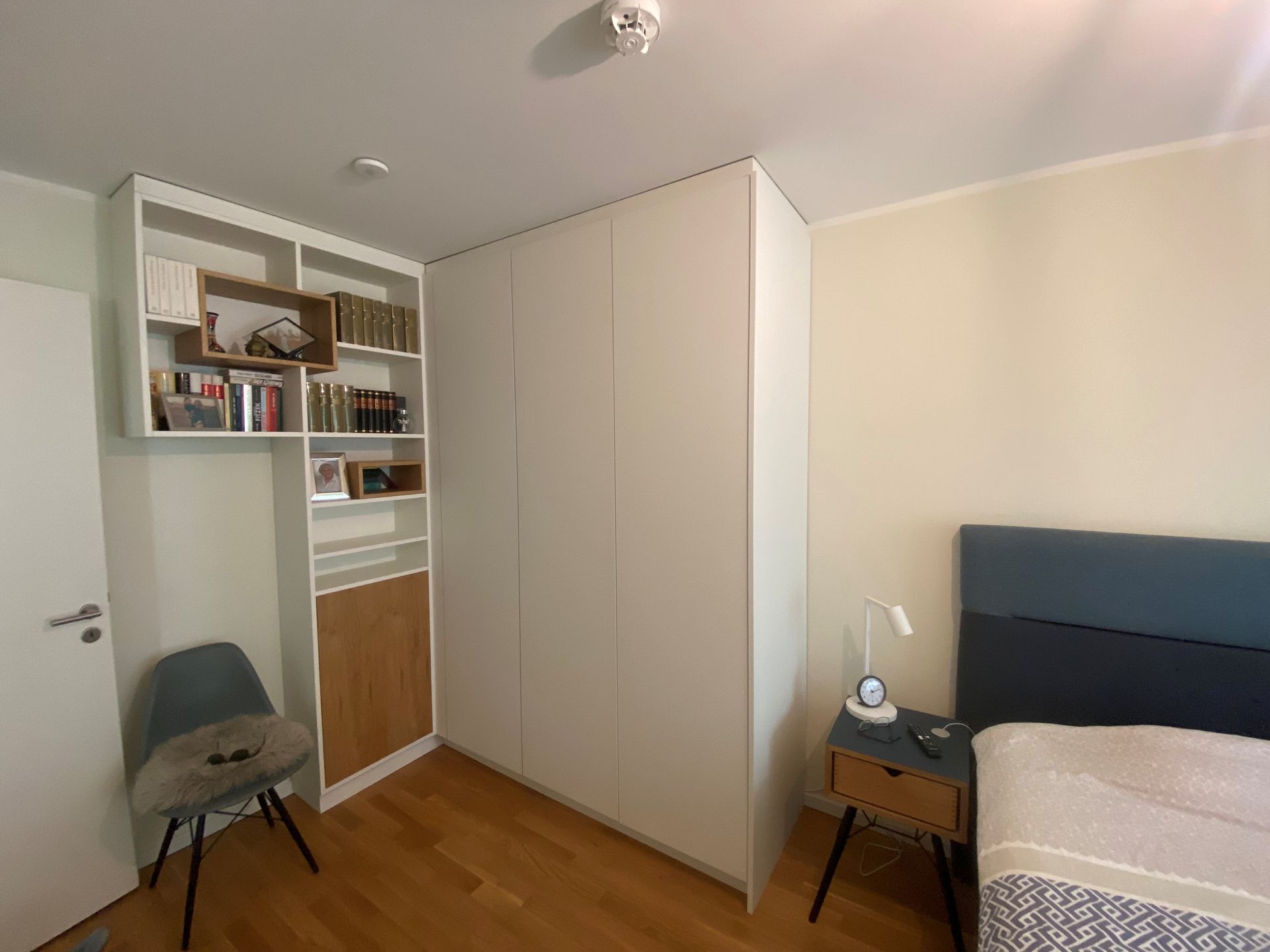 Ein Schlafzimmer mit Bett, Sessel, Nachttisch, Bücherregal und Kleiderschrank.