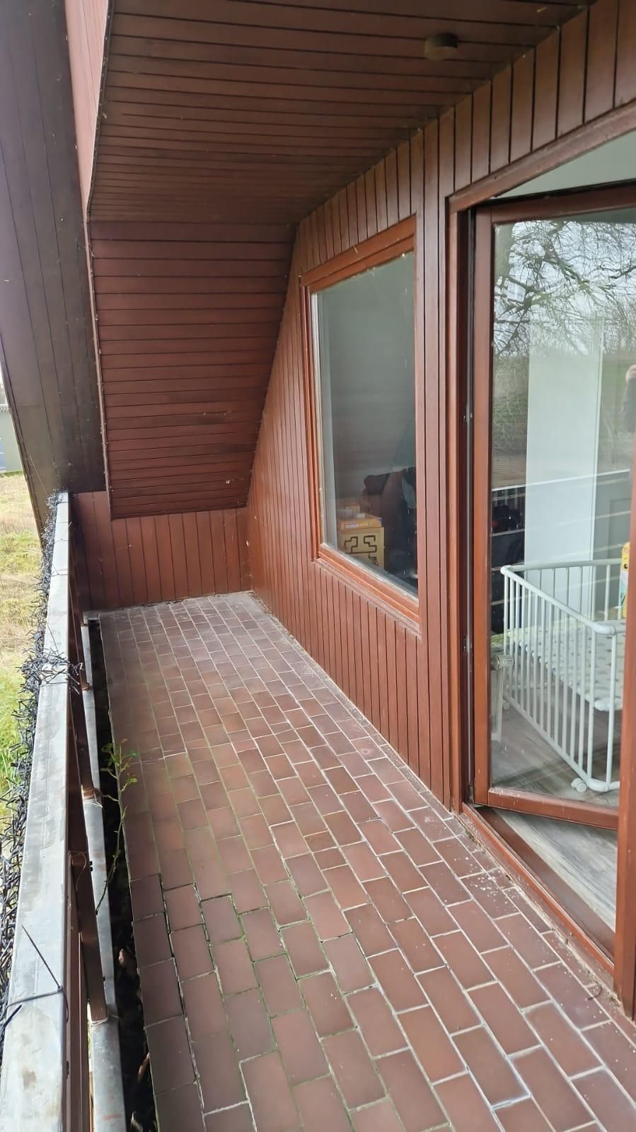 Ein Balkon mit Ziegelboden und großem Fenster.