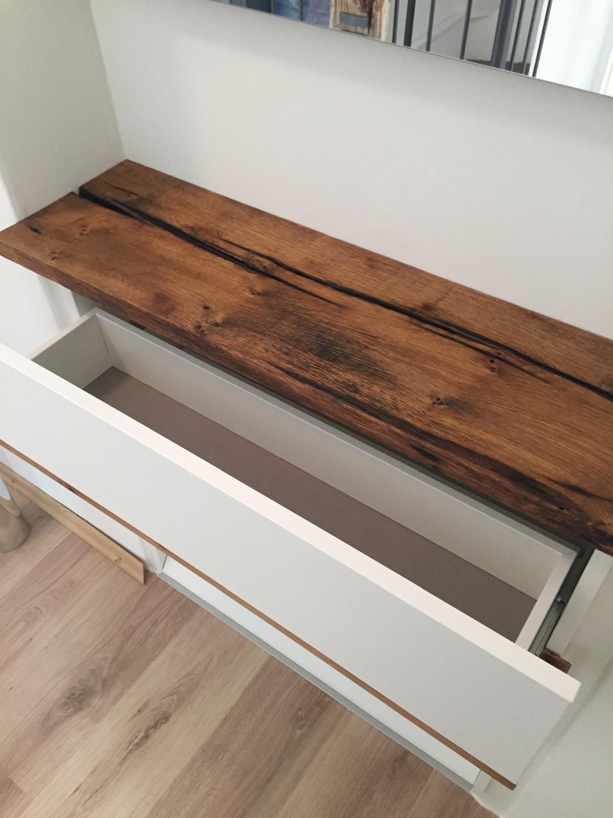 Auf einer weißen Schublade steht ein Holzregal.