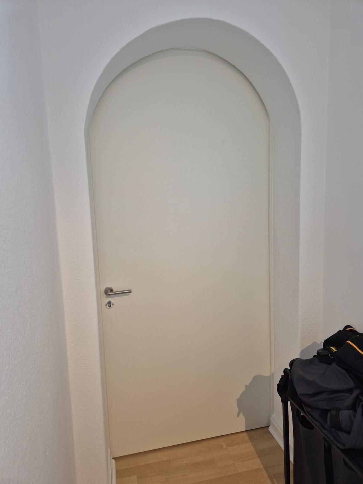 Eine weiße Tür mit einem geschwungenen Bogen in einem Flur.
