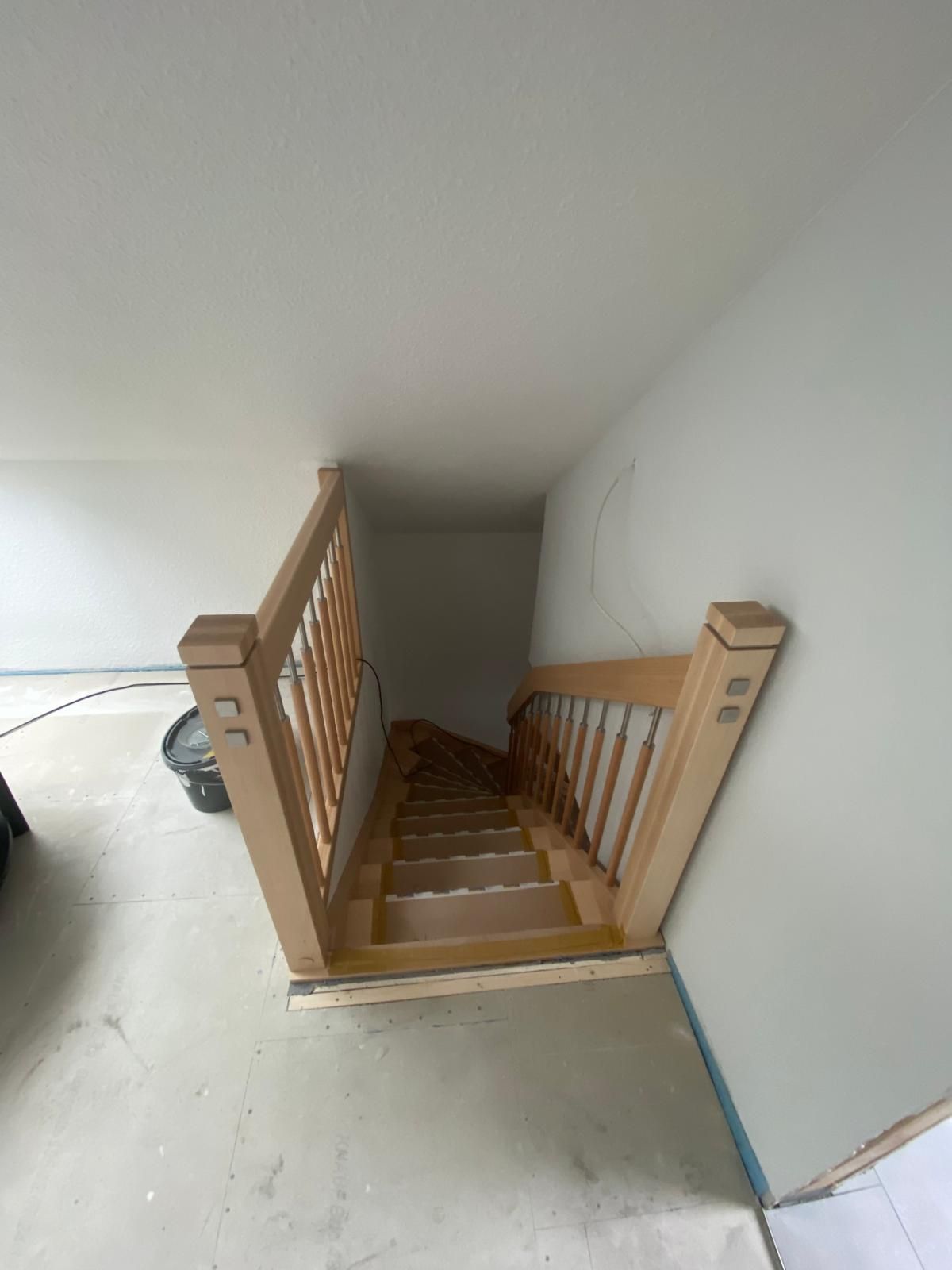 Eine Holztreppe führt in einem Raum eine weiße Wand hinauf.