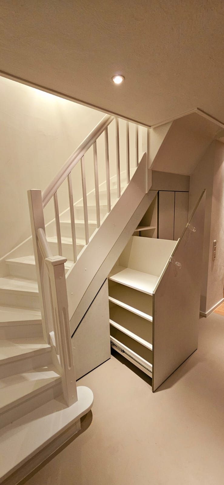Eine weiße Treppe mit einem eingebauten Regal darunter.