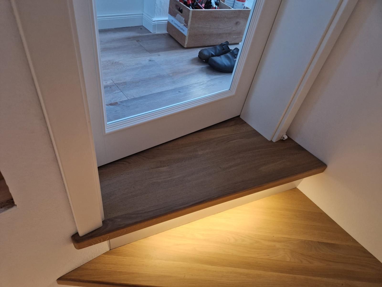 Eine Holztreppe mit einem Licht darunter und einer Tür.