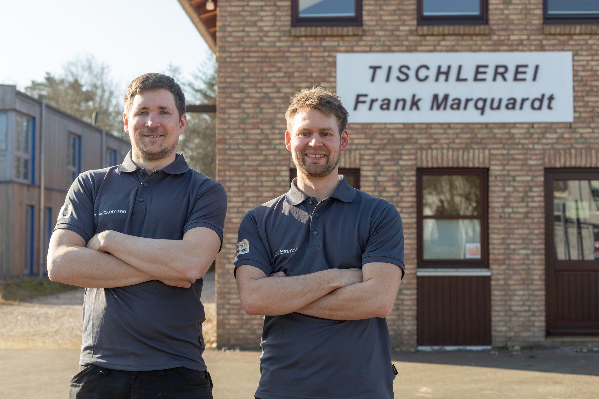 Zwei Männer stehen mit verschränkten Armen vor einem Gebäude.
