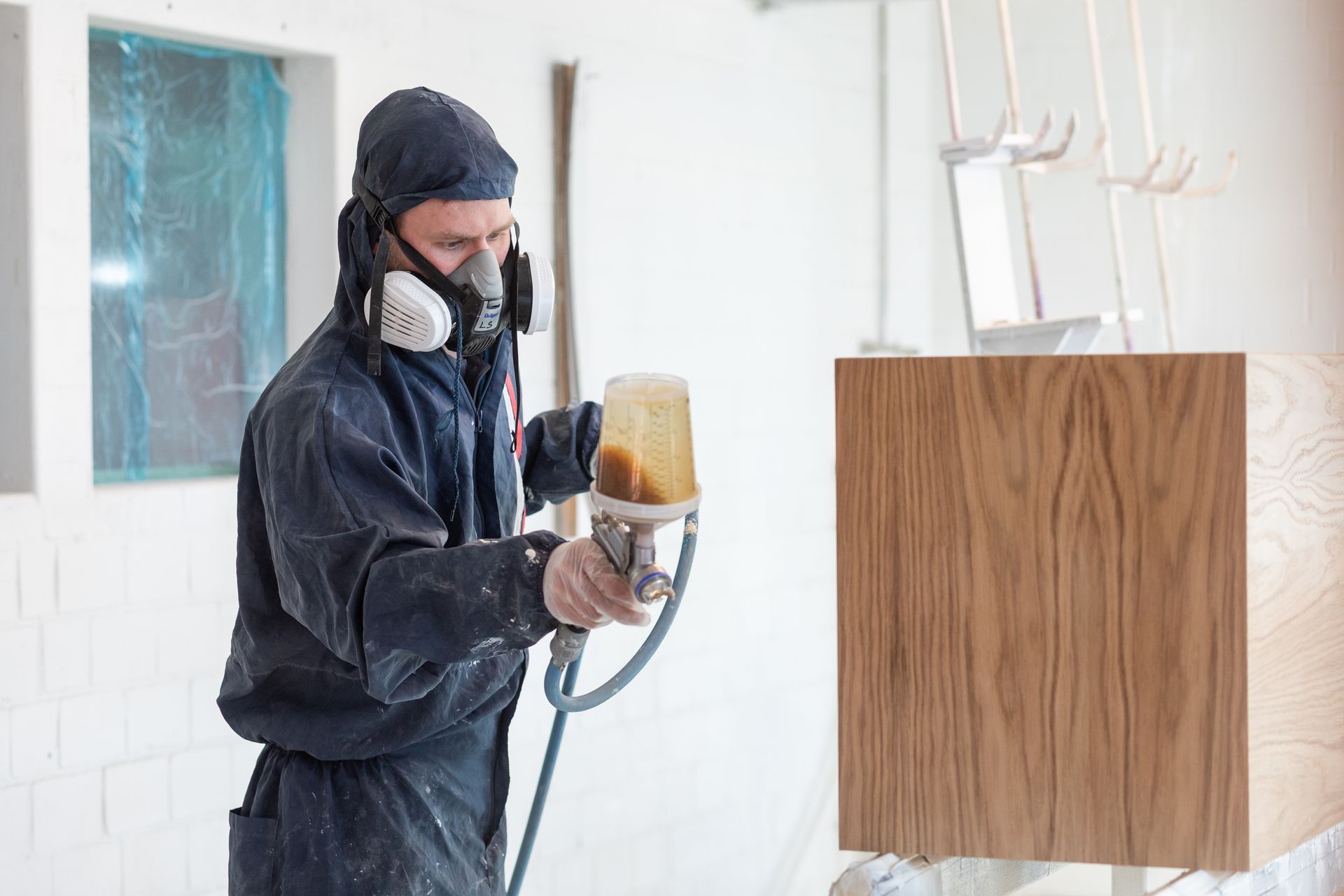 Ein Mann mit einer Maske besprüht eine Holzoberfläche mit Farbe.