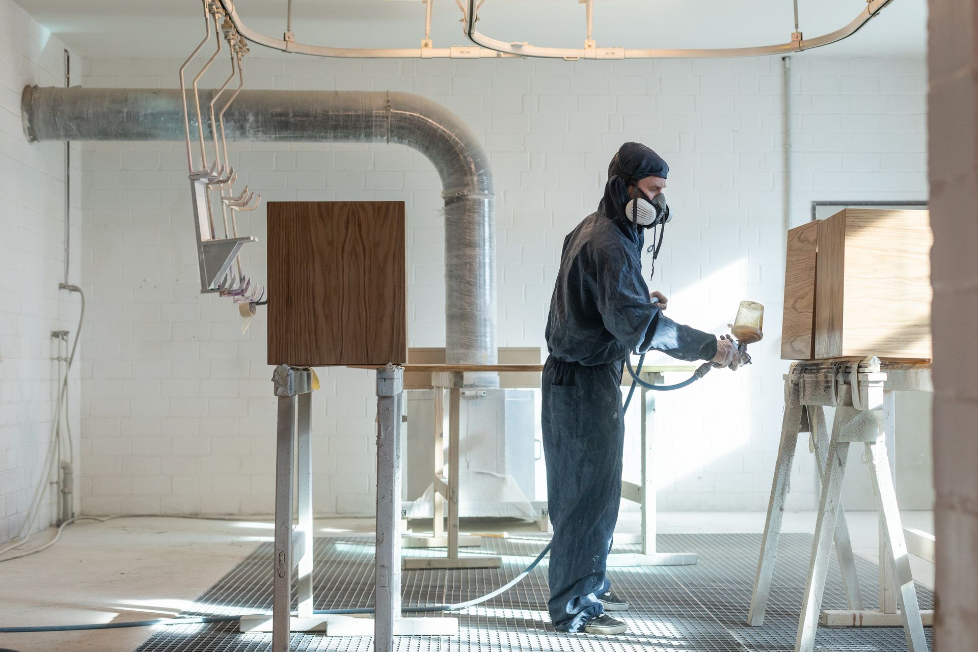Ein Mann mit einer Maske besprüht eine Holzkiste in einem Raum mit Farbe.