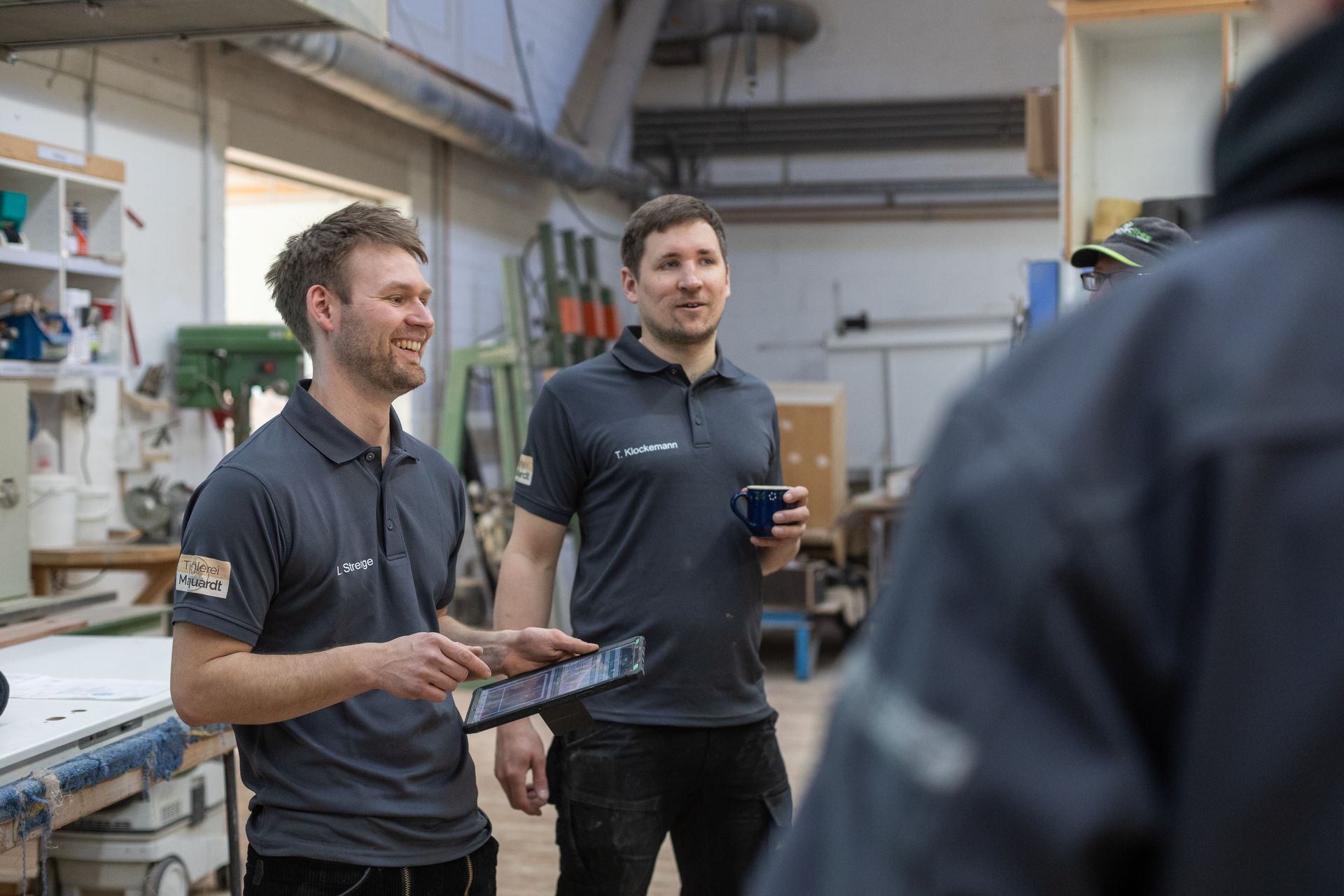 Zwei Männer stehen in einer Werkstatt und unterhalten sich.