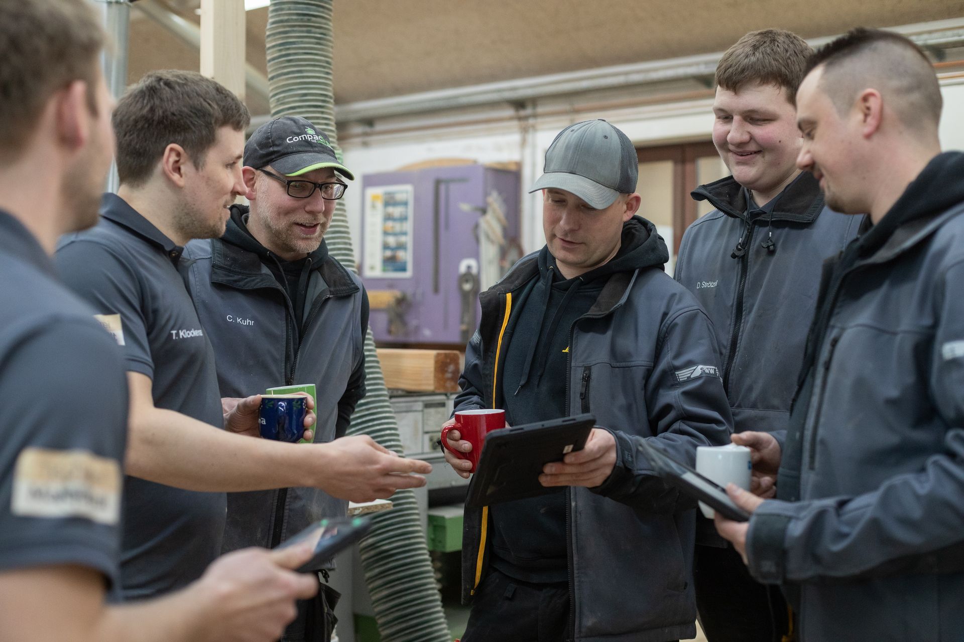 Eine Gruppe von Männern steht herum und schaut auf ein Tablet.