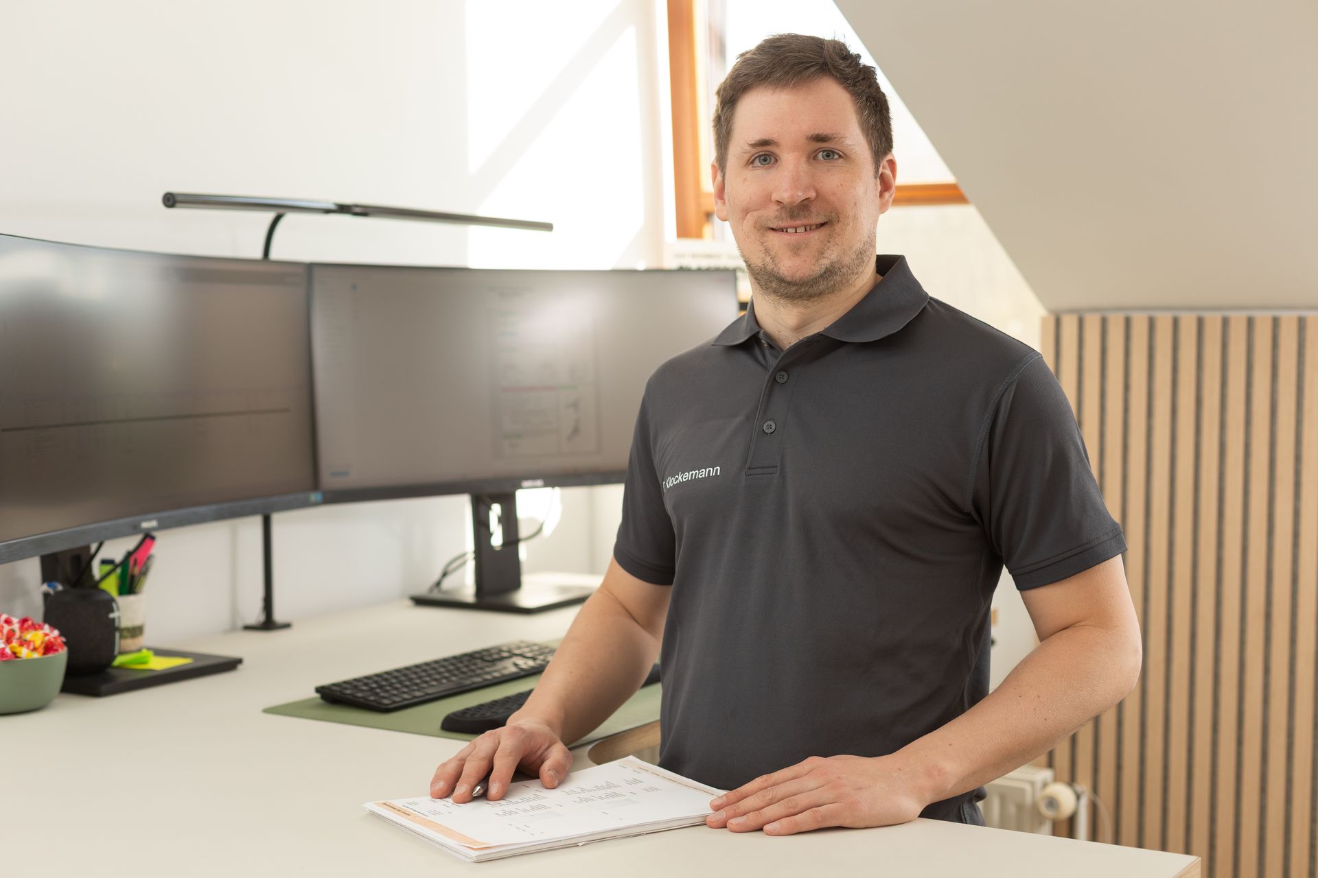 Ein Mann in einem Poloshirt steht vor einem Computertisch.