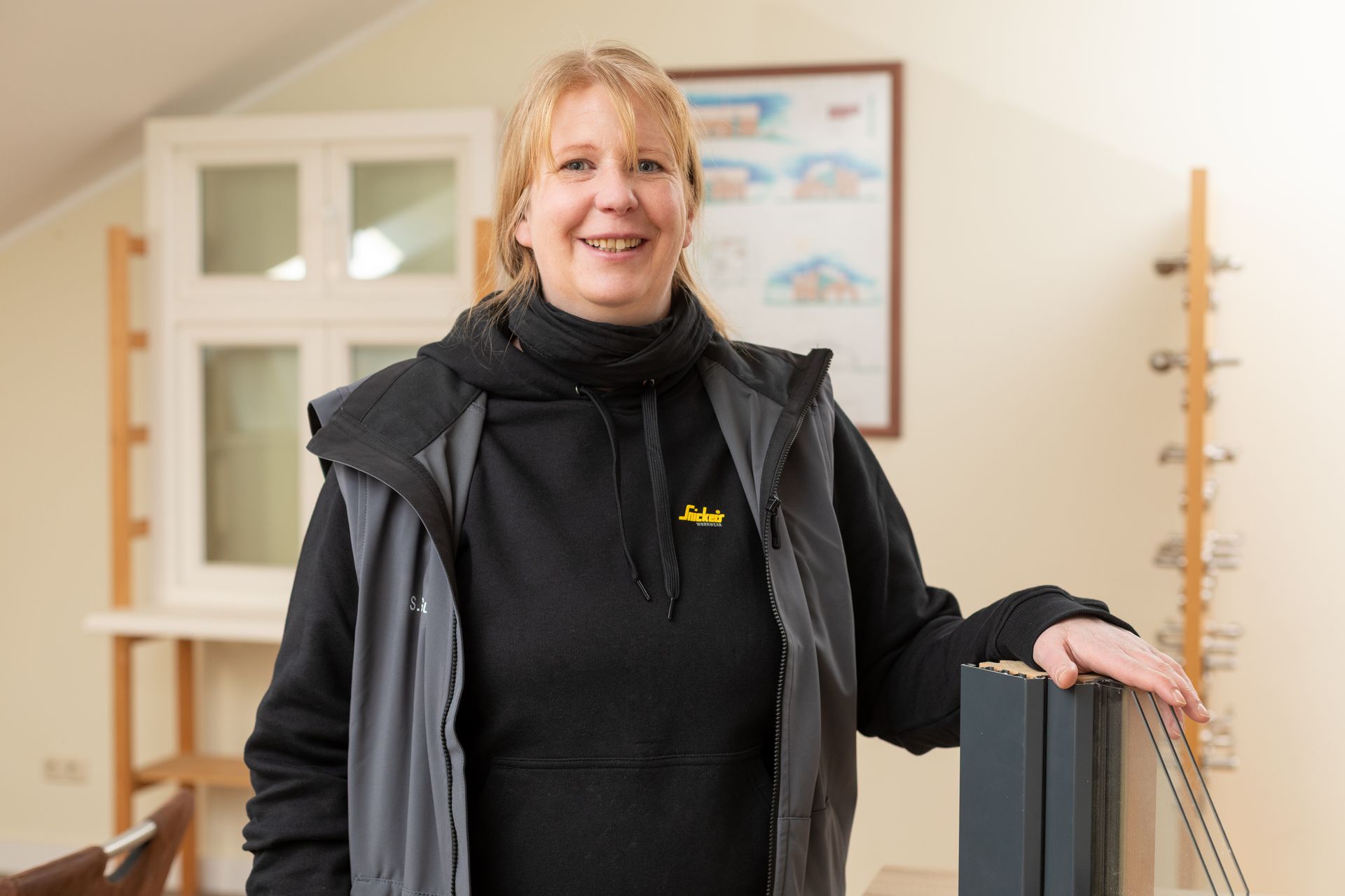 Eine Frau in einer schwarzen Jacke steht neben einem Fenster.