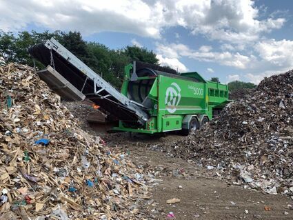 Eine grüne Maschine steht vor einem Müllhaufen.