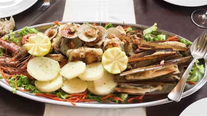 Plato de mariscos en bandeja de plata, con camarones, almejas, patatas y rodajas de limón.