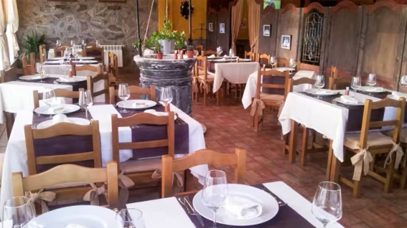 Comedor de restaurante con mesas preparadas para el servicio, sillas marrones, manteles blancos y pared de ladrillo.
