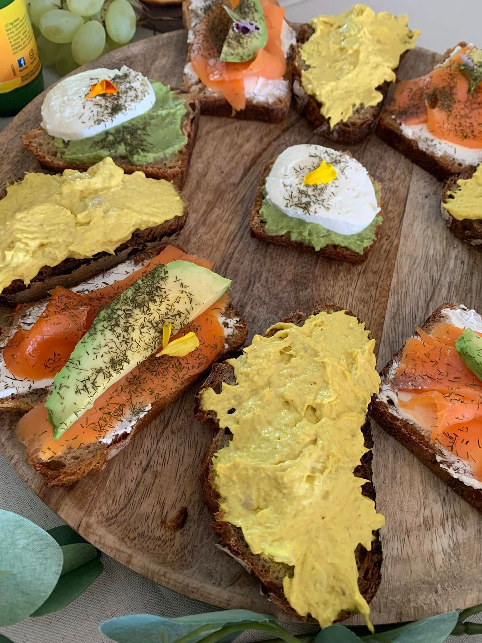 Tranches de pain grillé garnies de saumon, d'avocat, d'œufs et de pâte à tartiner jaune, servies sur une planche en bois.