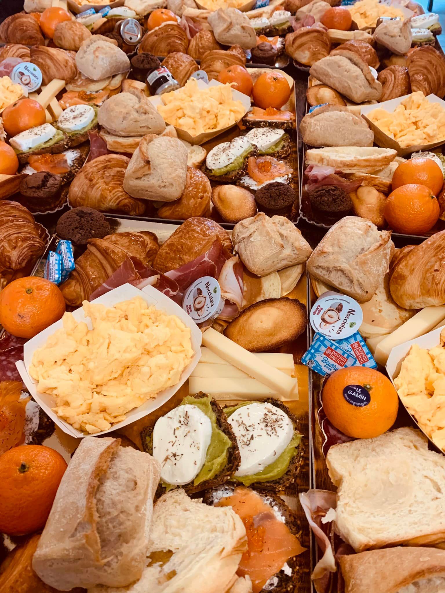 Assortiment de produits pour le petit-déjeuner : pain, croissants, œufs brouillés, mandarines, fromage et viennoiseries.