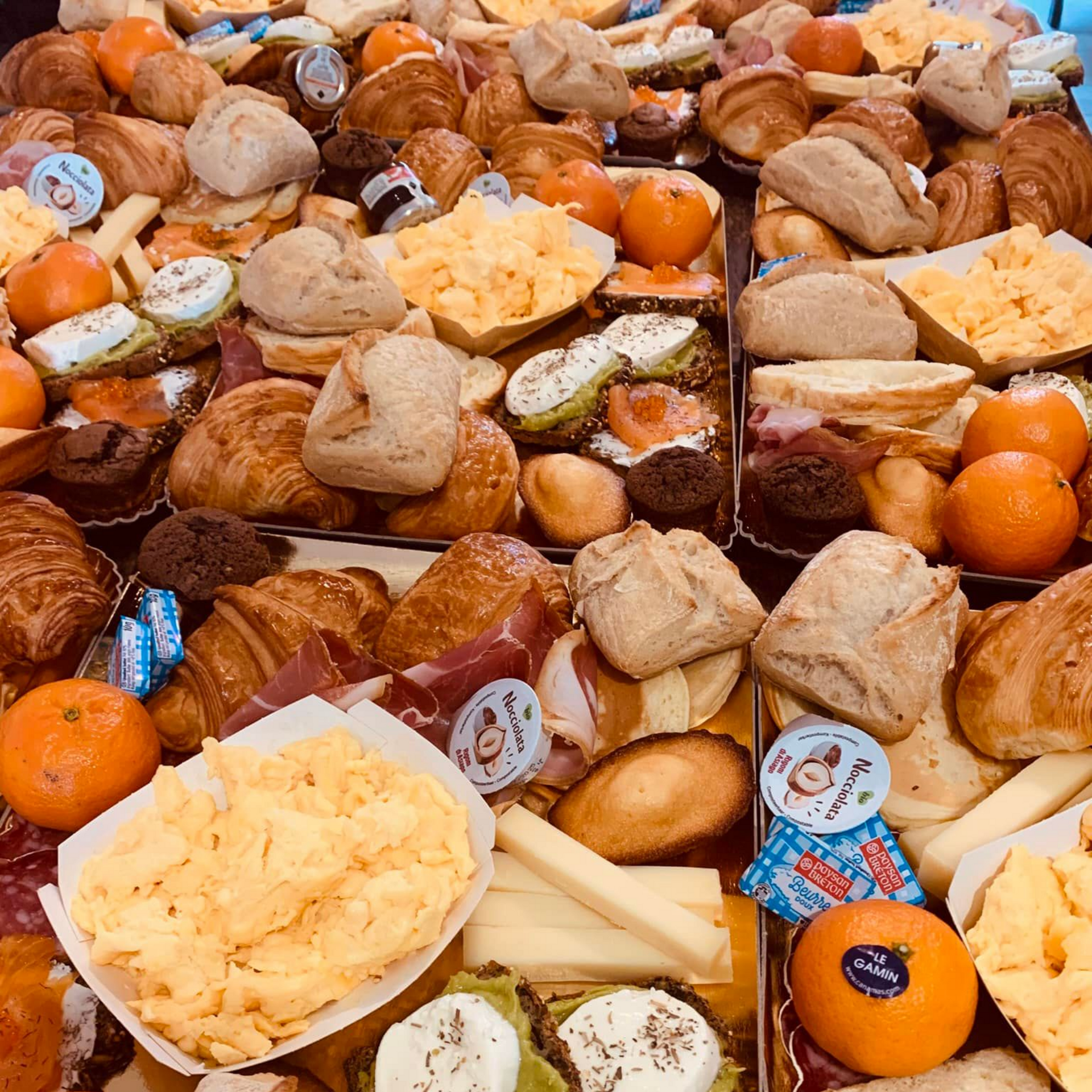 Gros plan sur un assortiment de produits pour le petit-déjeuner : viennoiseries, œufs brouillés, mandarines, pain et fromage.