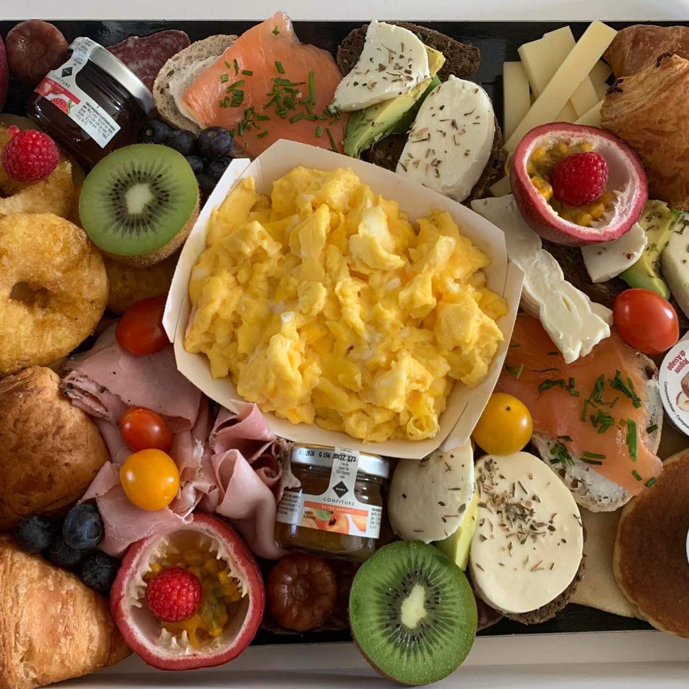 Assiette de petit déjeuner avec œufs brouillés, fruits, viennoiseries, saumon fumé et fromage.