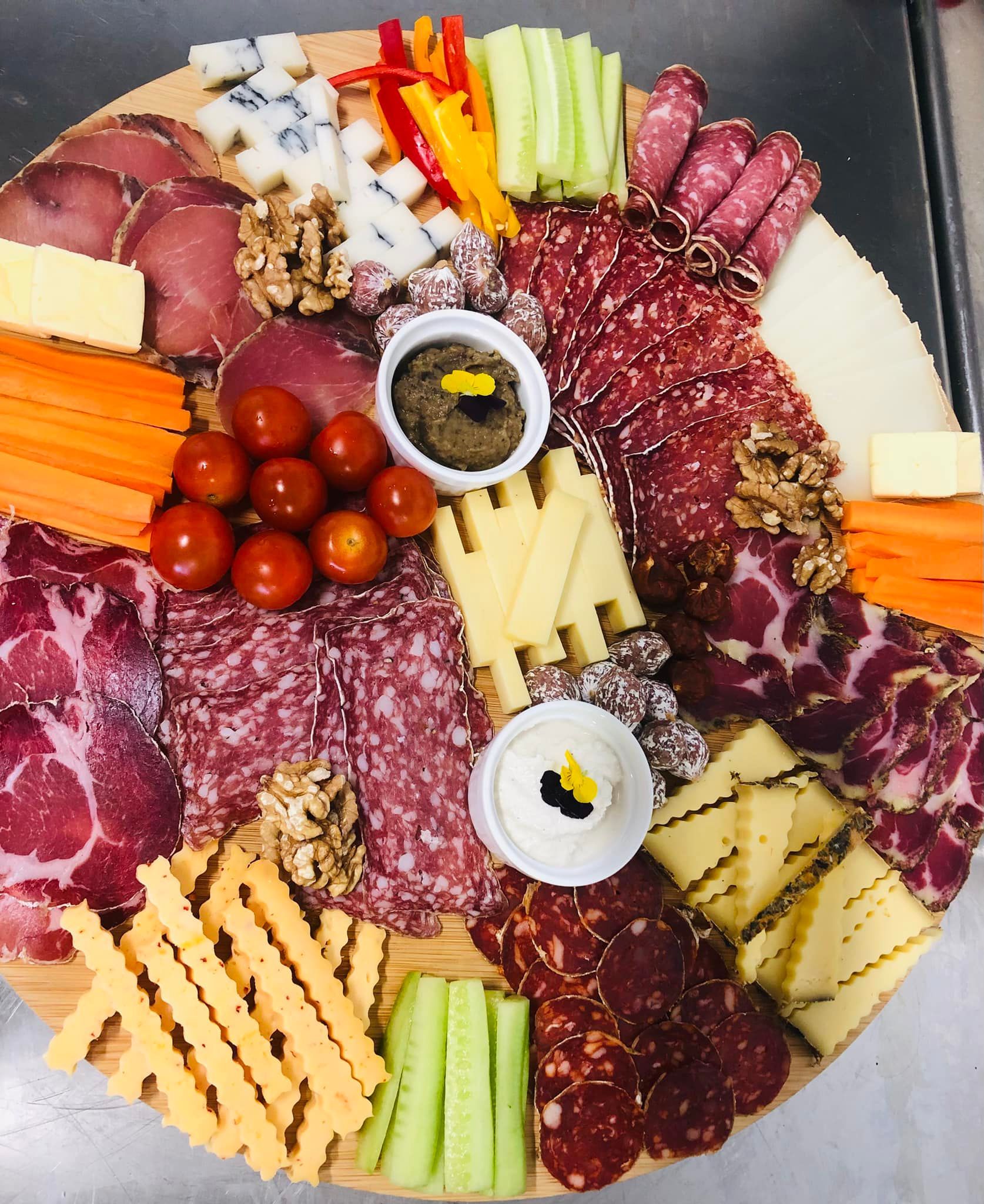 Planche de charcuterie : viandes, fromages, légumes, noix et sauces disposés sur un plateau en bois.