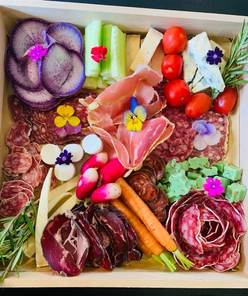 Planche de charcuterie avec pommes de terre violettes, tomates, salami, prosciutto, fromage, radis et carottes.