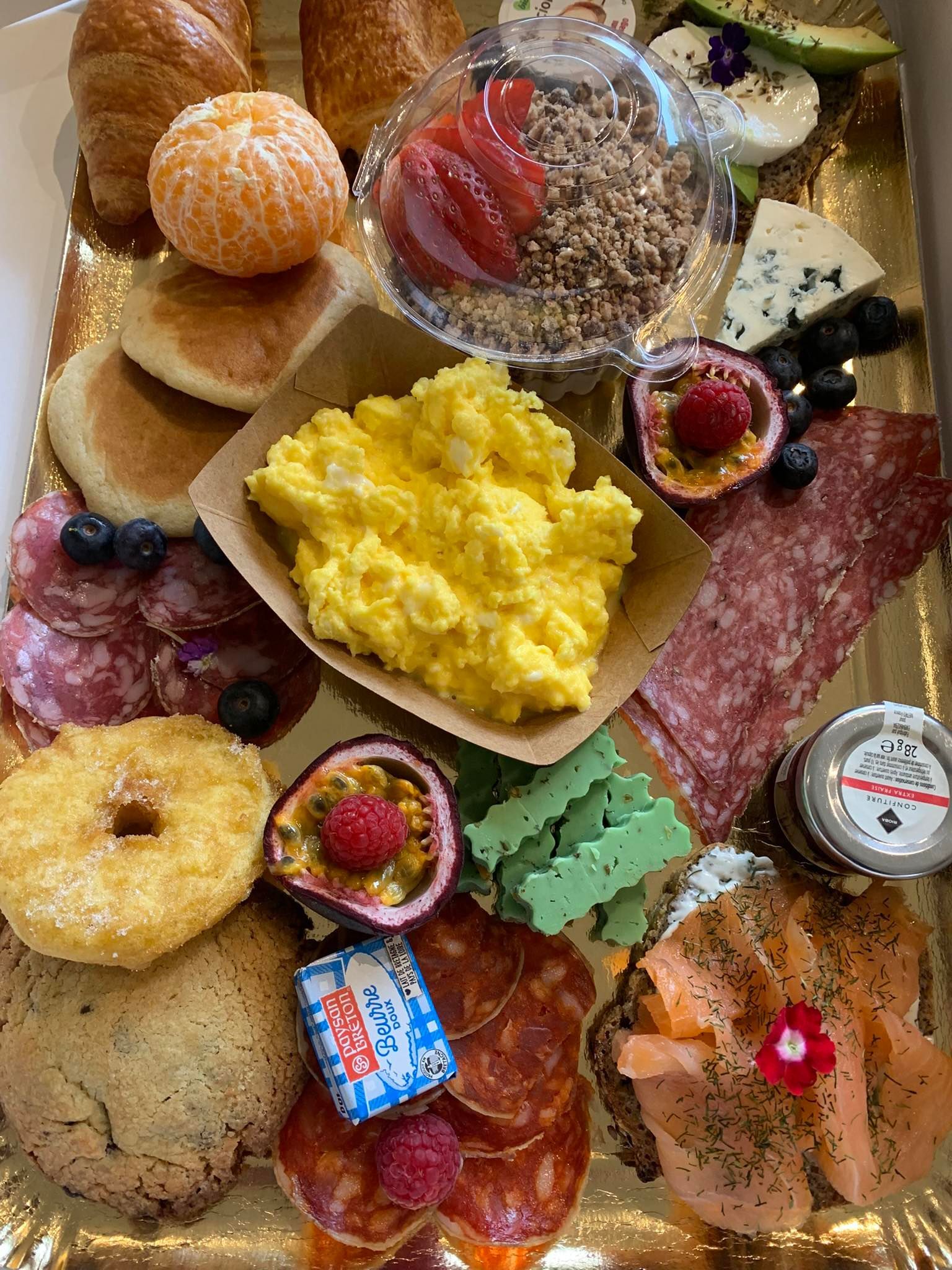 Assiette de petit déjeuner avec œufs brouillés, croissants, salami, fruits, fromage et viennoiseries.