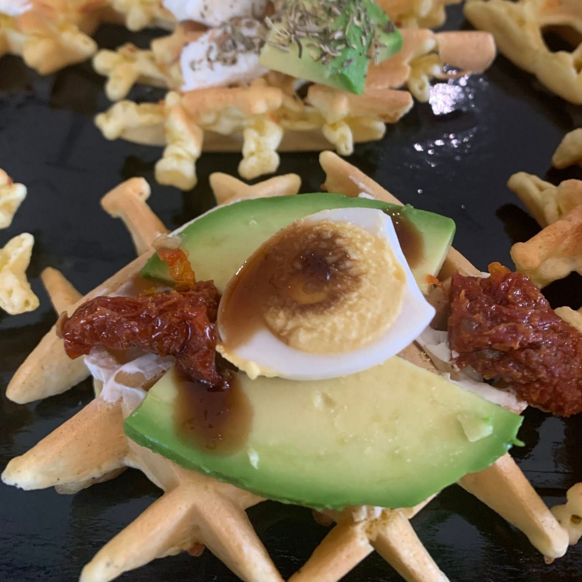 Gaufre garnie d'avocat, d'œuf, de tomates séchées et de sauce.