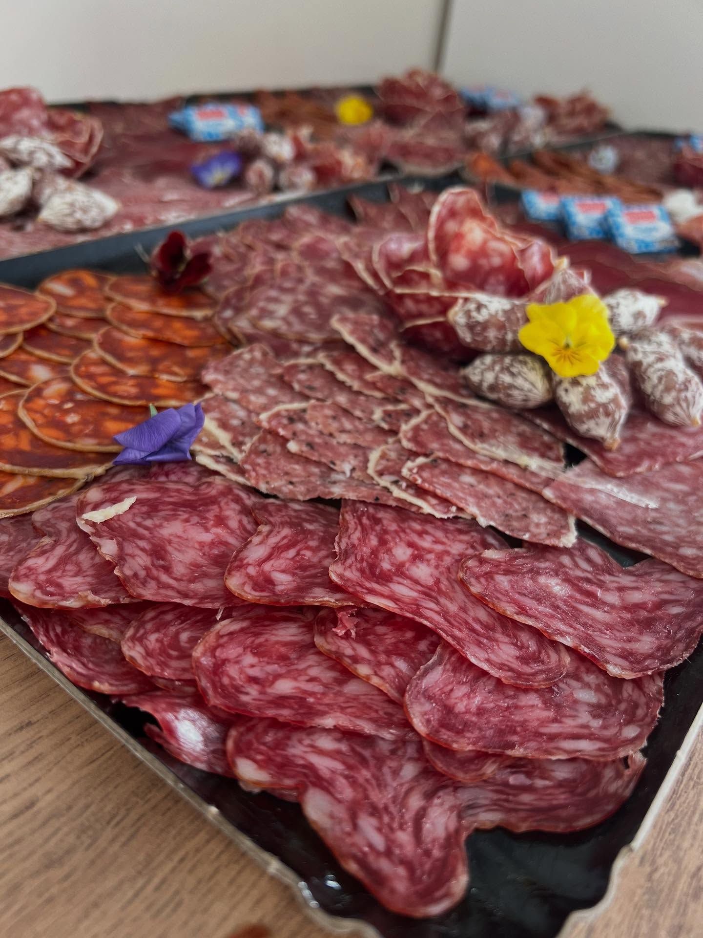 Planche de charcuterie composée de diverses viandes tranchées, dont du salami et du chorizo, décorée de fleurs.