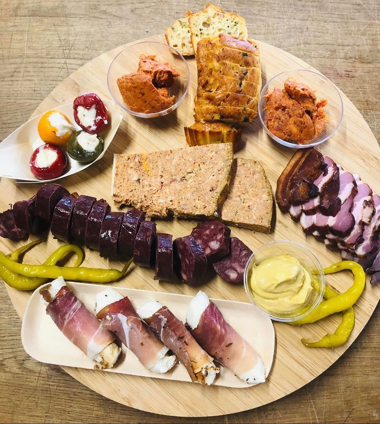Planche en bois garnie de charcuterie assortie : viande, fromage, poivrons et condiments.