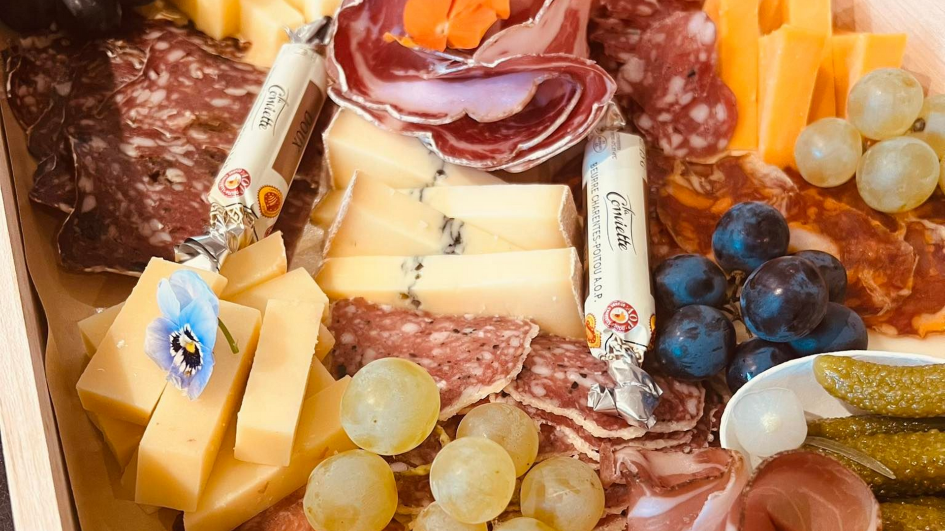 Planche de charcuterie avec fromages, viandes, raisins et cornichons.