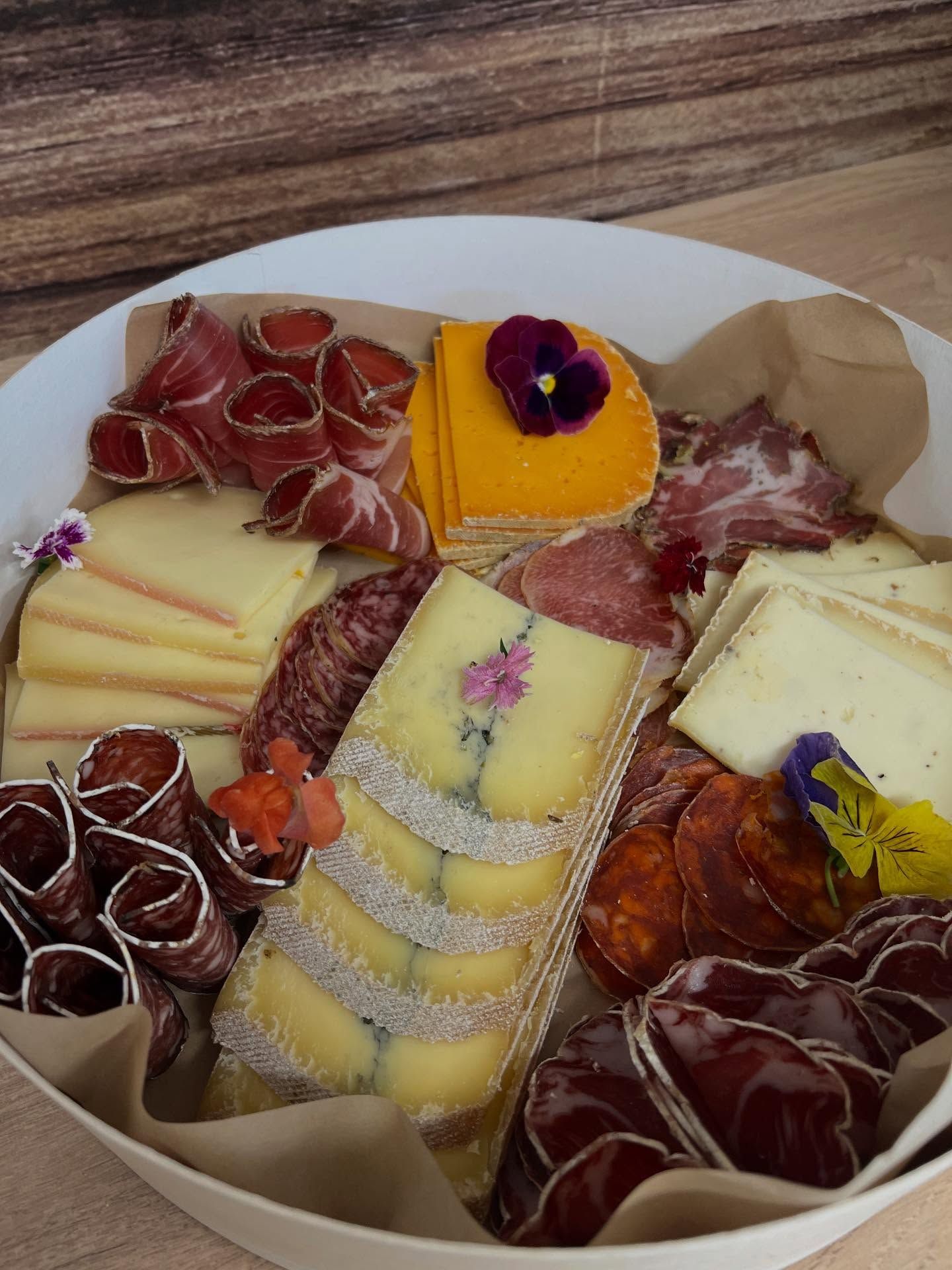 Planche de charcuterie composée de fromages, de viandes et de crackers variés, décorée de fleurs comestibles.