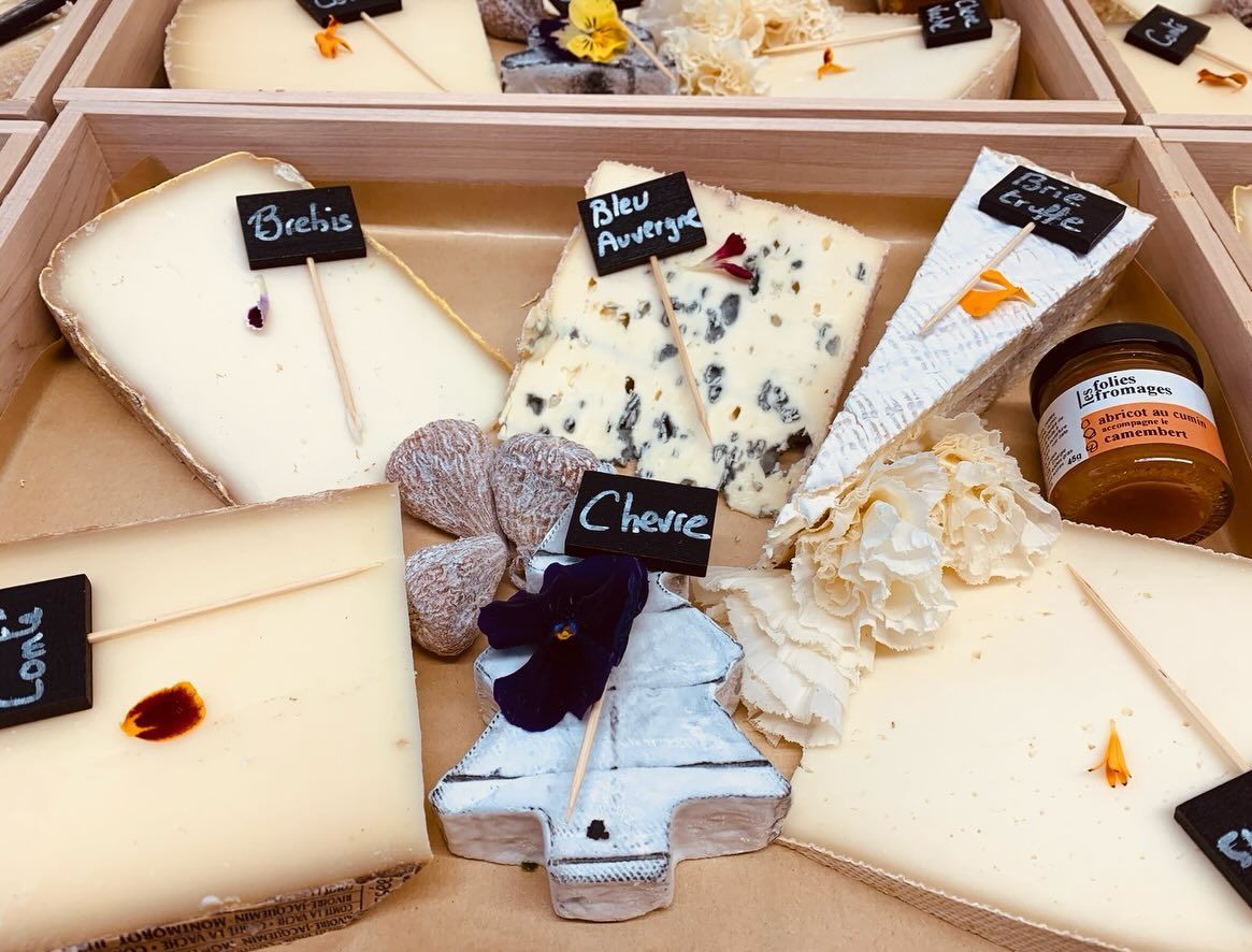 Assortiment de fromages artisanaux étiquetés, présentés dans des plateaux en bois. Comprend du fromage bleu et un pot de confiture.