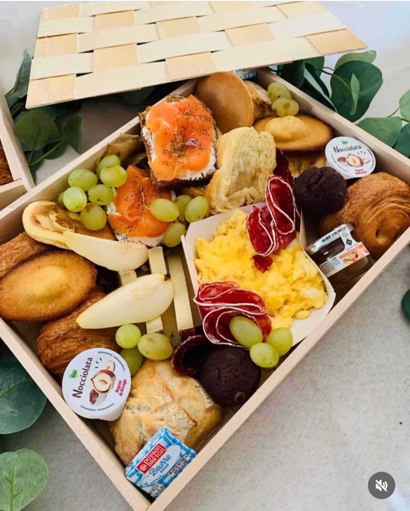 Plateau de petit déjeuner avec saumon fumé, œufs, fruits, viennoiseries et tartinades, présenté dans une boîte en bois.