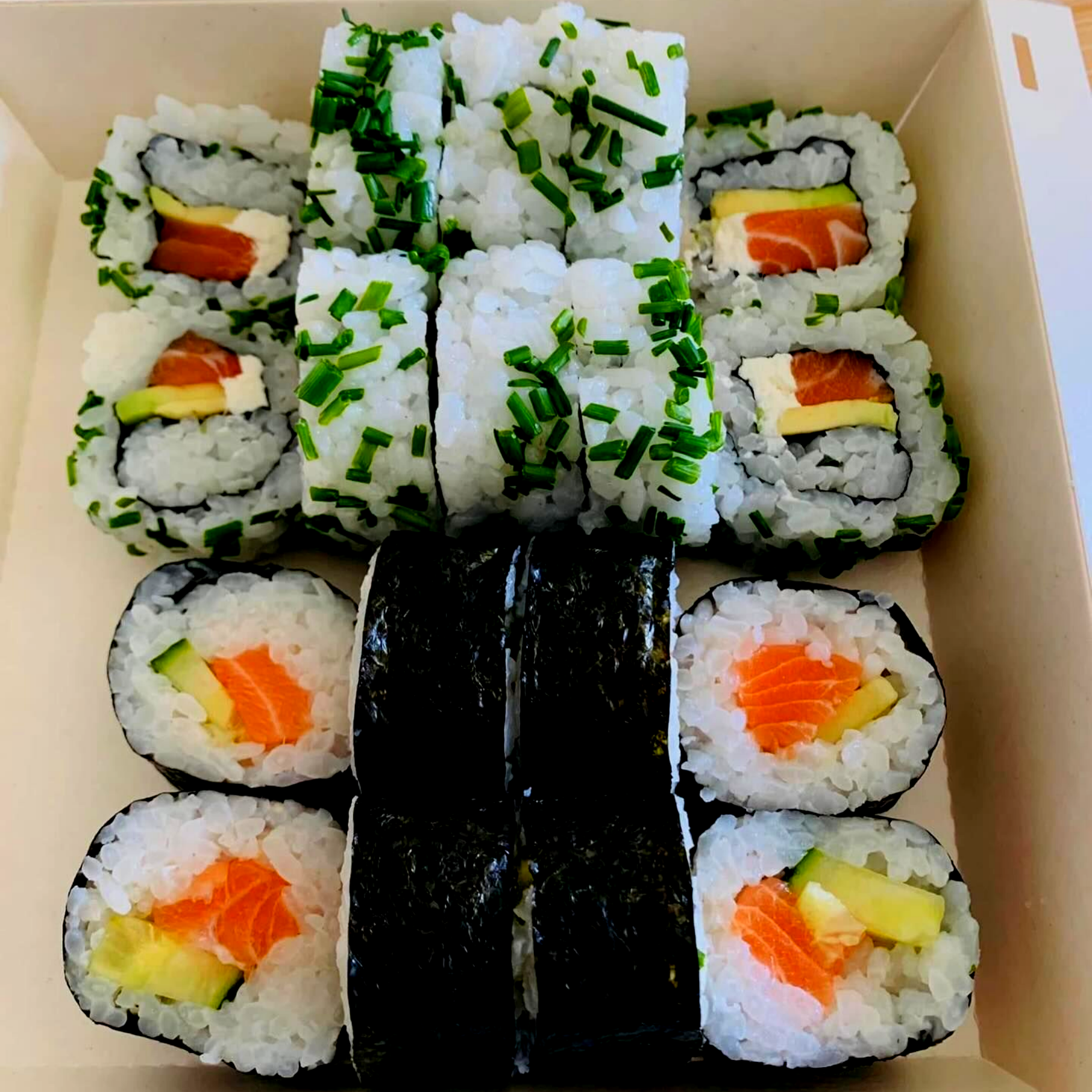 Rouleaux de sushi en boîte, comprenant du saumon, de l'avocat et de la ciboulette.