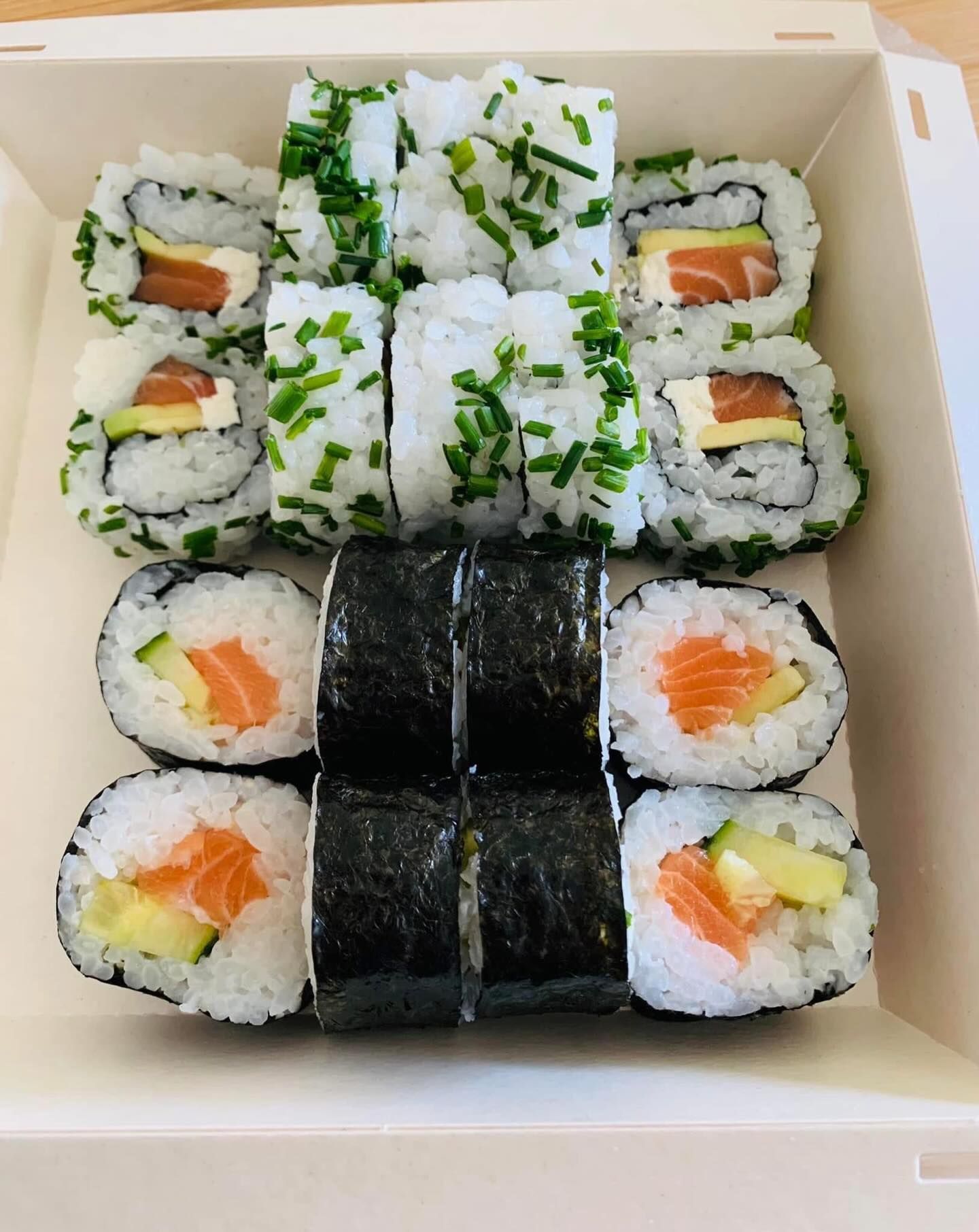 Rouleaux de sushis dans un contenant à emporter, comprenant du saumon, de l'avocat et de la ciboulette.