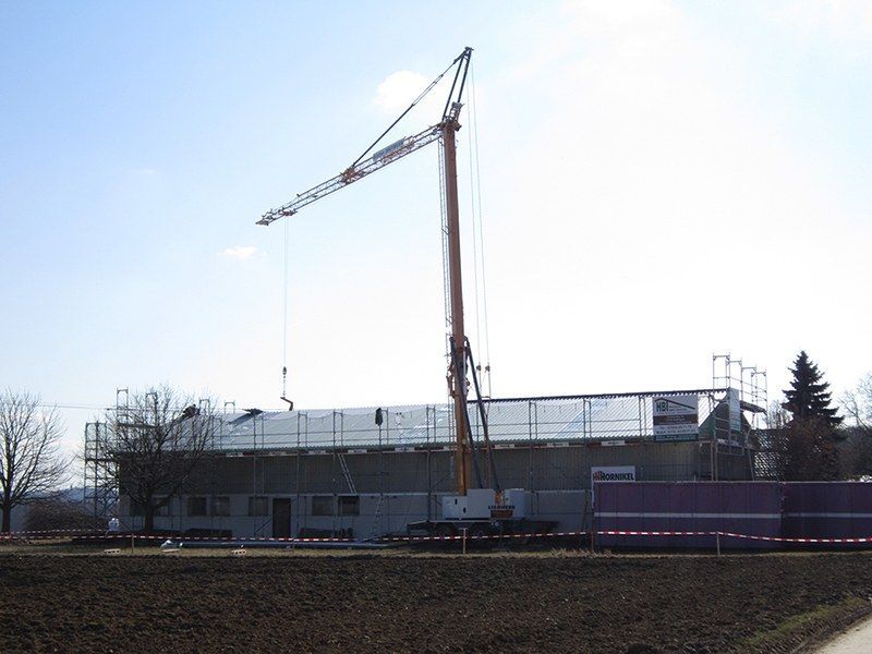 HB Holzbau Breymaier GmbH –
Kran ragt vor blauem Himmel über im Bau befindliches Gebäude